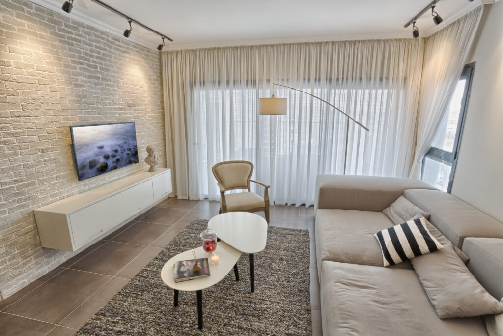 Cream curtains and sheer drapes in a modern Singapore living room with a sectional sofa and brick wall.