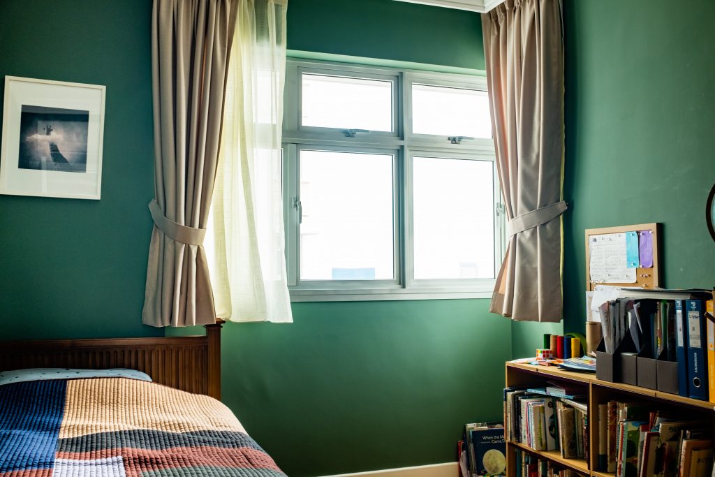 Taupe curtains in a cosy Singapore bedroom with sheer day drapes, green walls, and a study bookshelf.