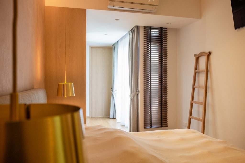 Grey curtains and dark wooden blinds in a cosy Singapore bedroom with warm lighting and minimalist decor.