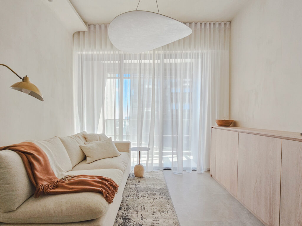 Sheer day curtains in a bright minimalist Singapore living room with a sofa, side table, and built-in cabinet.
